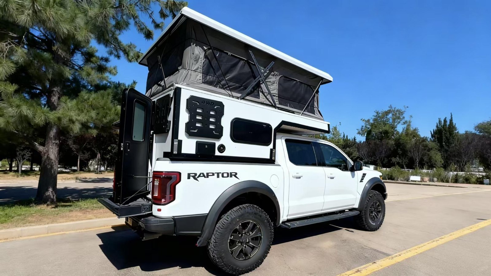 Hvit pickup camper med hevet pop-up-tak og åpen sidedør på en pickup