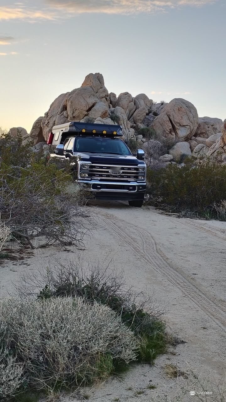 Pickup med pickup camper på grusvei mellom klipper